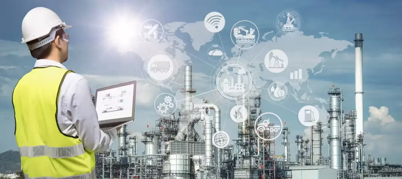 Industrial engineer with laptop overseeing oil refinery operations enhanced with digital IoT connectivity icons.