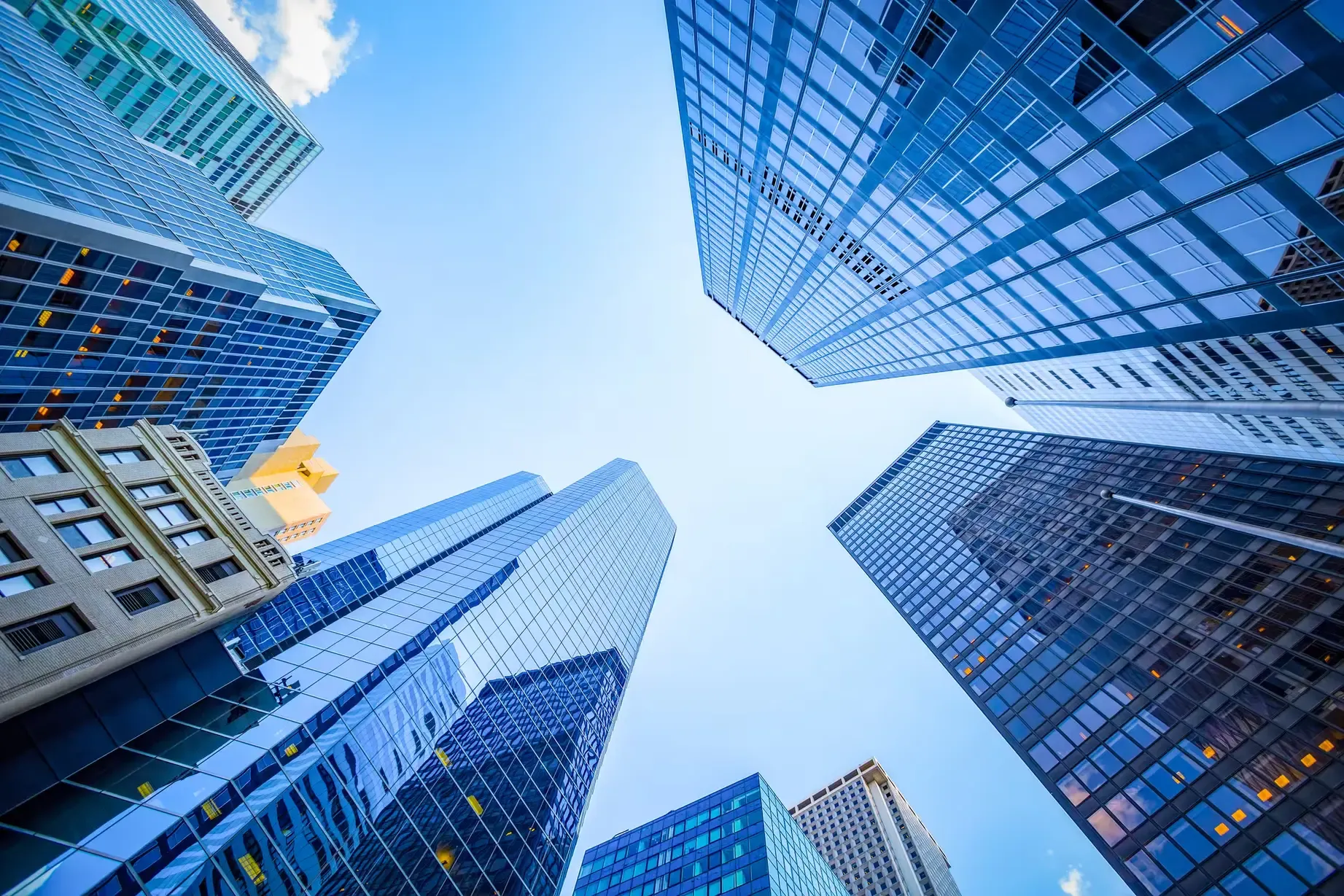 Upward view of towering skyscrapers with reflective glass facades under a vibrant blue sky, symbolizing urban growth and architecture.